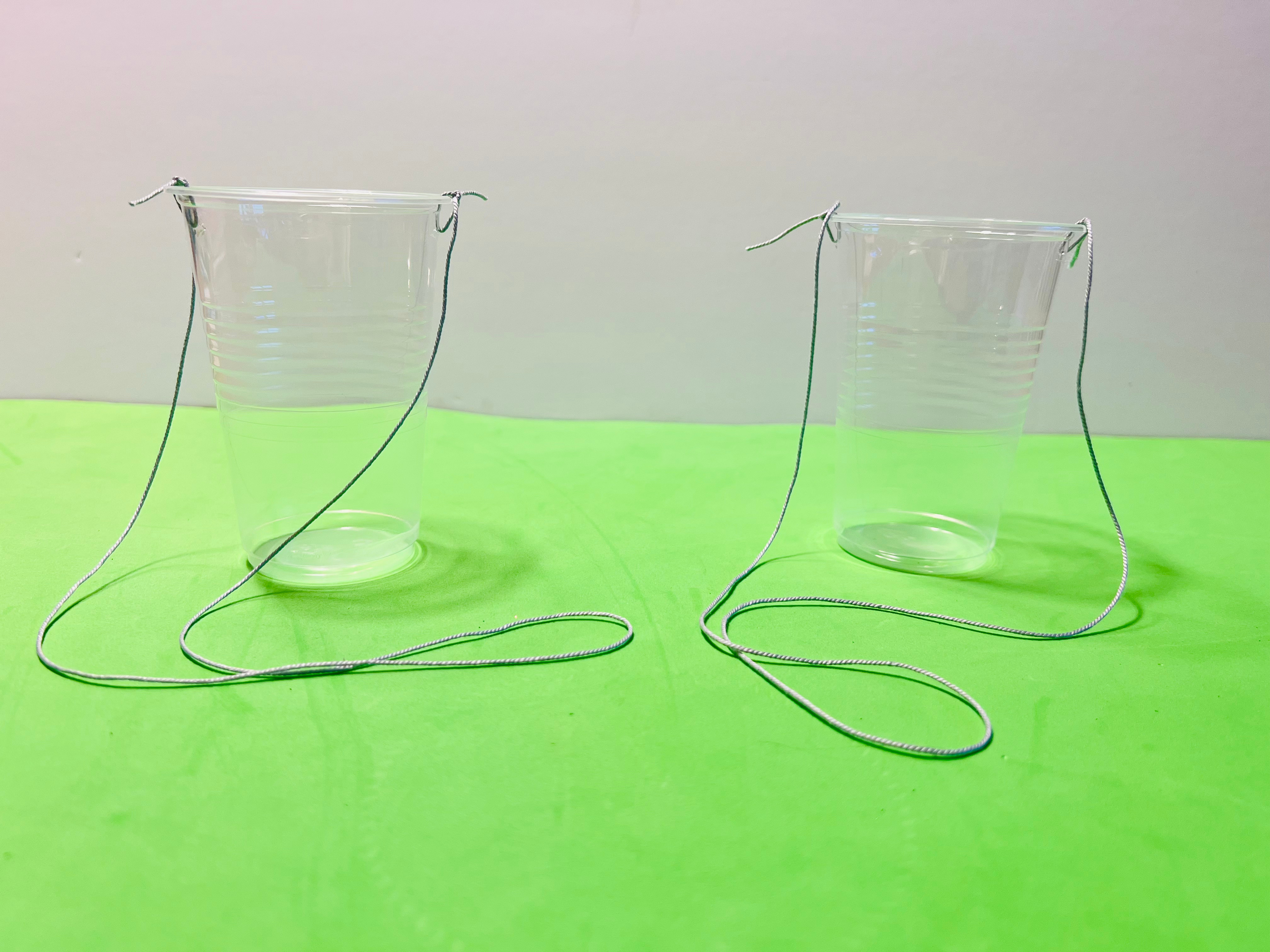 two empty plastic cups, each with a string tied to its sides like a bucket