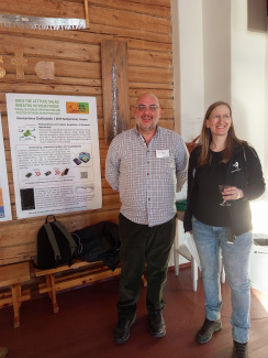 two persons standing in front of a project poster that is hanging on a wall with wooden panelling