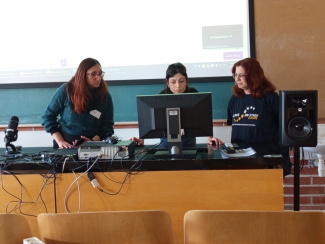 three persons standing in a lecture room, looking at a computer