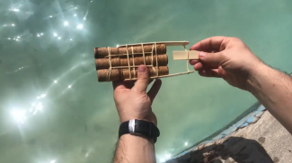 A person is holding a boat made of nine corks with a propeller made of a flat stick and a twisted rubber band.