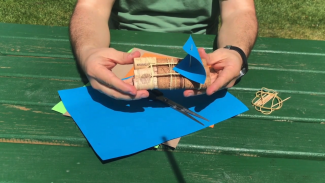 A person is holding a boat made of nine corks with a sail made of blue paper.